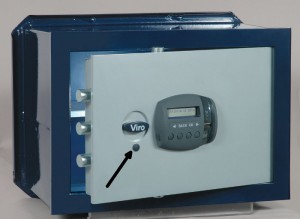 La freccia indica il tappo di protezione della serratura di sicurezza che si può usare per aprire la cassaforte se le batterie si esauriscono.